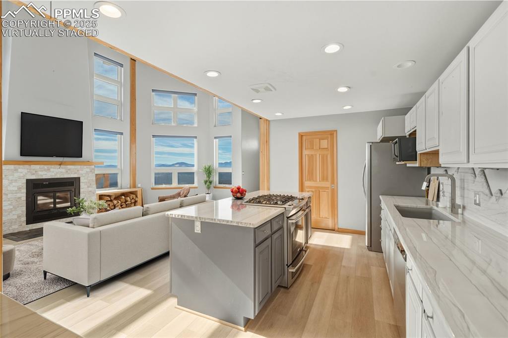 Virtually Staged - Kitchen featuring white cabinets, light stone countertops, recessed lighting, appliances with stainless steel finishes, and a kitchen island