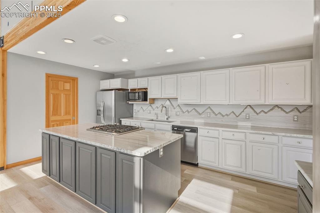 Kitchen featuring white cabinets, decorative backsplash, light wood-style floors, and recessed lighting