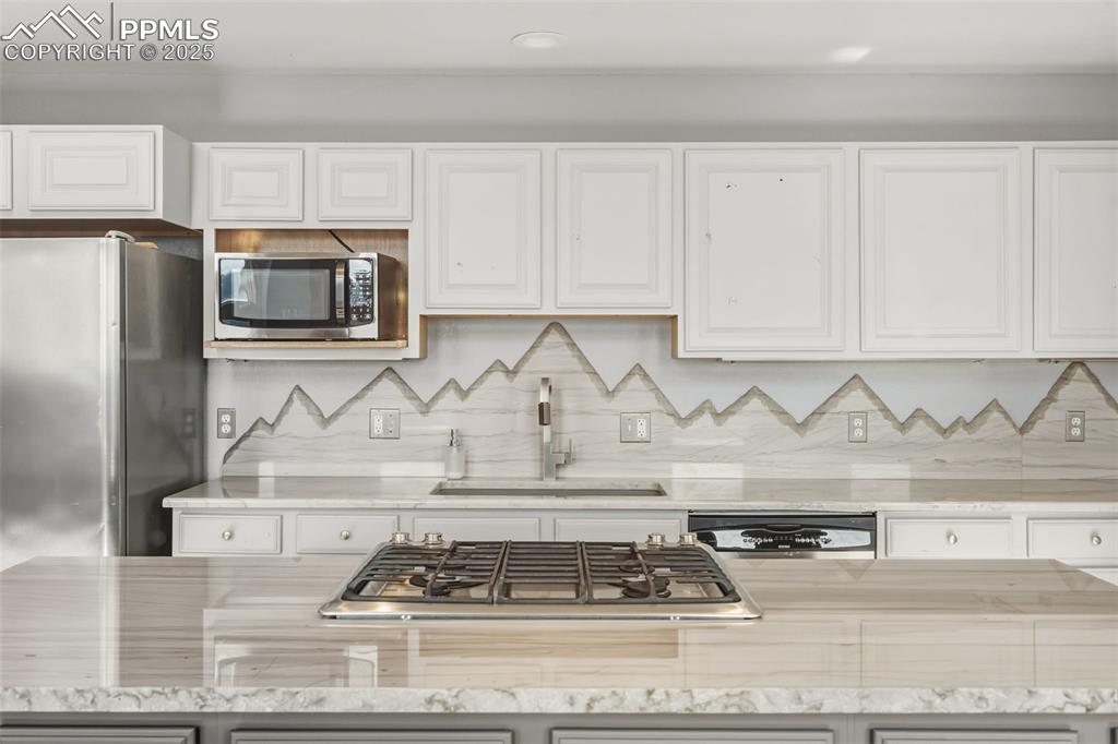 Kitchen with light stone counters, stainless steel appliances, white cabinetry, and backsplash