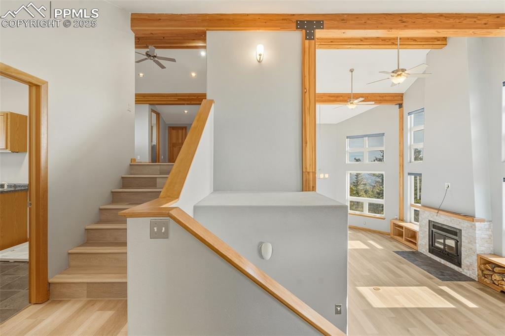 Stairway featuring beam ceiling, wood finished floors, a ceiling fan, a fireplace with flush hearth, and high vaulted ceiling