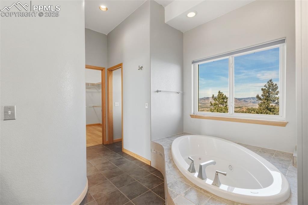 Full bathroom with a spacious closet, a jetted tub, a mountain view, recessed lighting, and dark tile patterned flooring