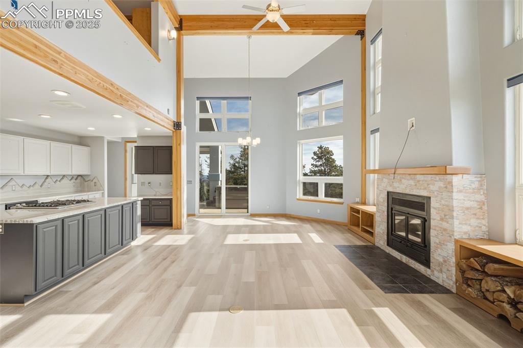 Kitchen featuring beam ceiling, white cabinets, tasteful backsplash, light wood finished floors, and a fireplace