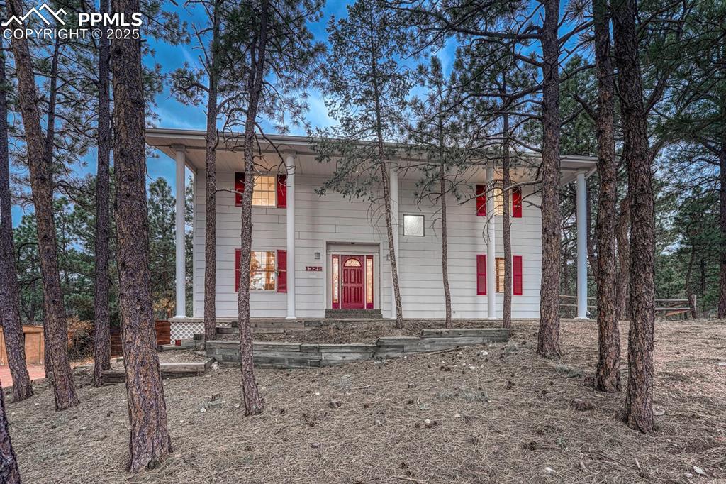 Front of home with terraced planter beds and mature trees.