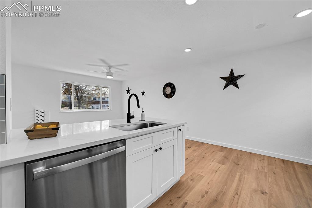 Kitchen with stainless steel dishwasher, white cabinets, light wood-style floors, recessed lighting, and light stone counters