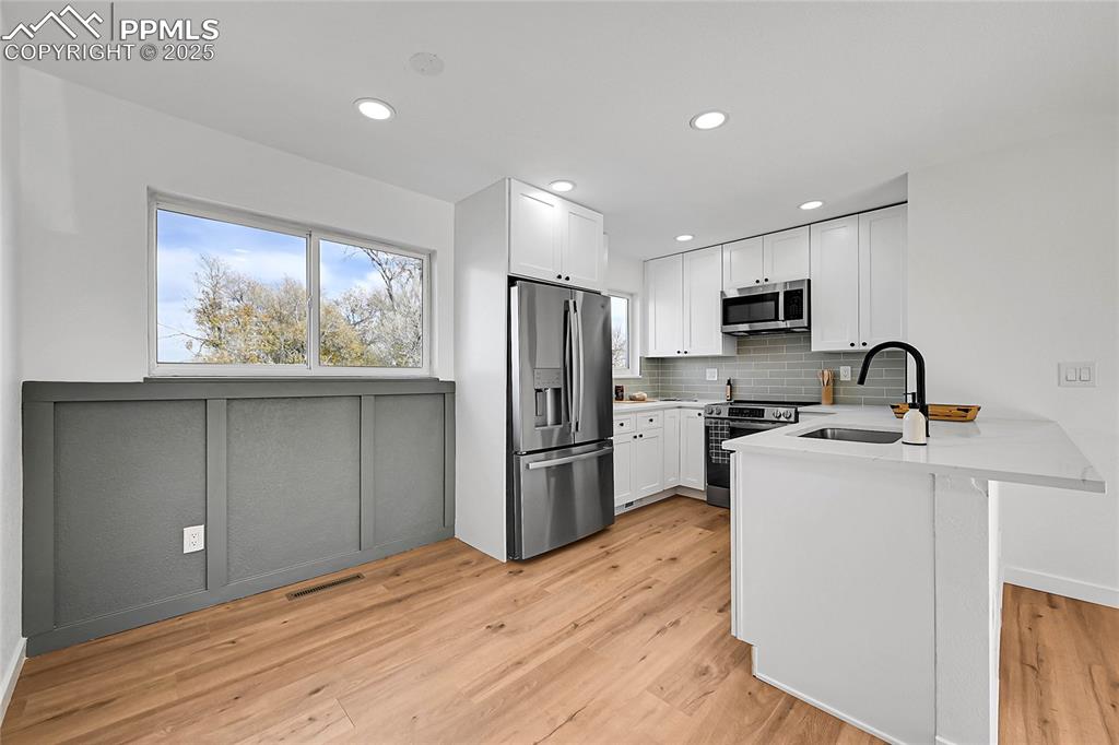 Kitchen featuring a peninsula, healthy amount of natural light, stainless steel appliances, white cabinetry, and recessed lighting
