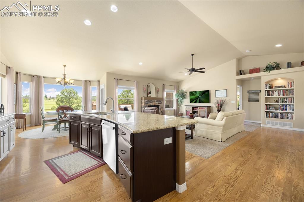 Kitchen with stainless steel dishwasher, a chandelier, a stone fireplace, dark brown cabinetry, and vaulted ceiling