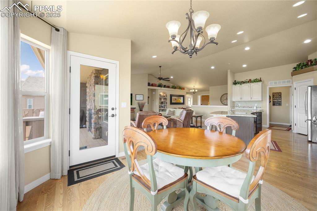 Dining space featuring a ceiling fan, a chandelier, vaulted ceiling, light wood-style flooring, and recessed lighting