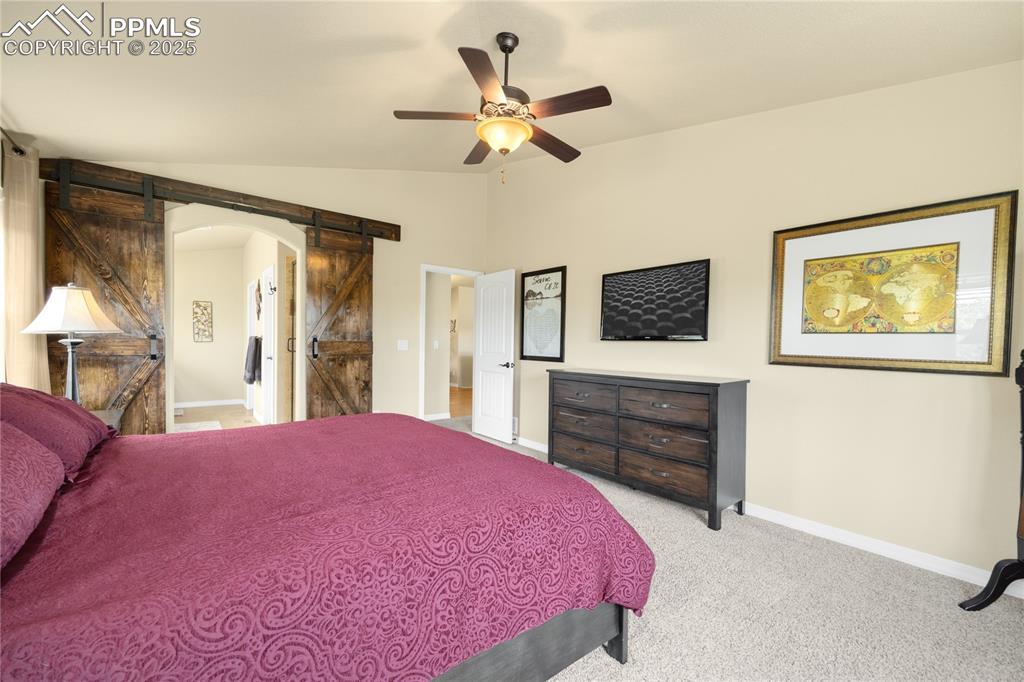 Bedroom with a barn door, lofted ceiling, light carpet, arched walkways, and a ceiling fan