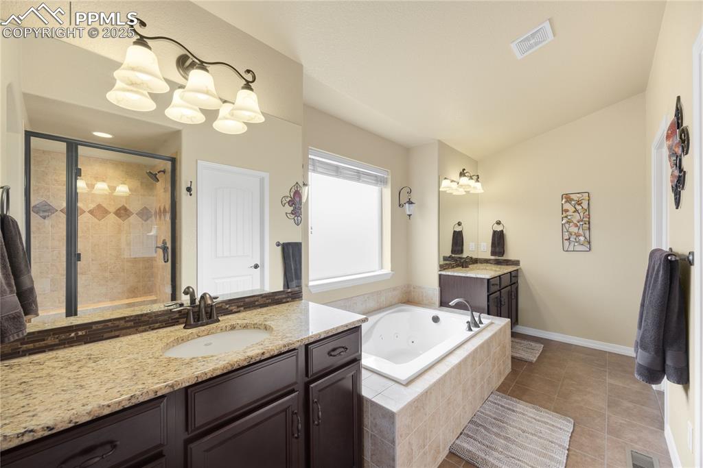 Full bathroom with a stall shower, a jetted tub, two vanities, vaulted ceiling, and tile patterned flooring