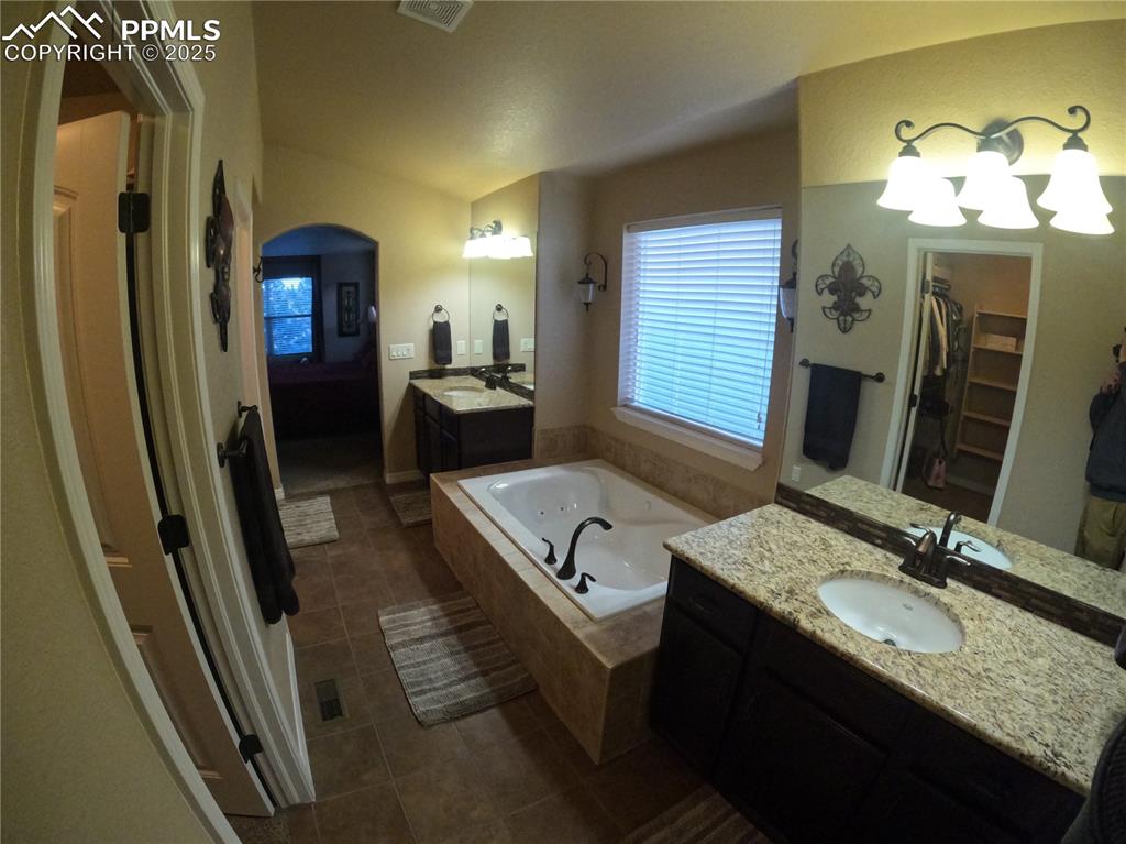 Primary Bathroom with two vanities, a garden tub, a walk in closet, and dark tile patterned flooring