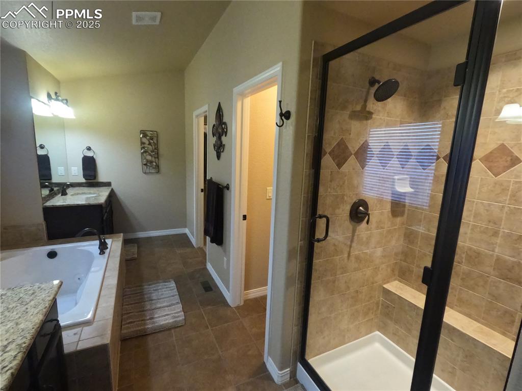 Primary Full bathroom with vanity, a garden tub, a stall shower, and dark tile patterned flooring