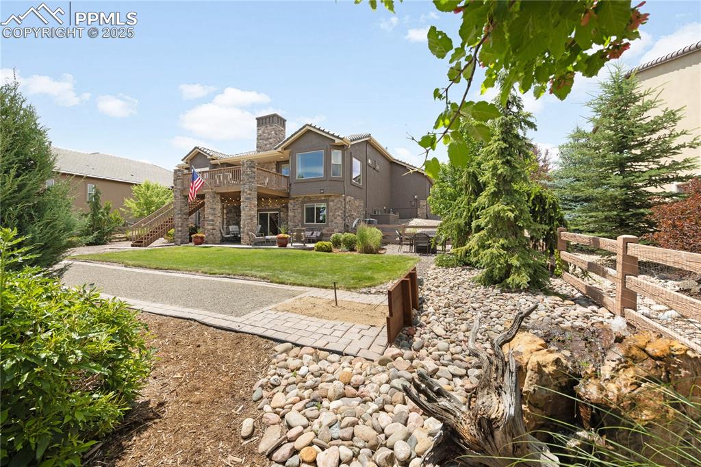 View of rear of home featuring a chimney, stairway, a patio, a wooden deck, and stone siding