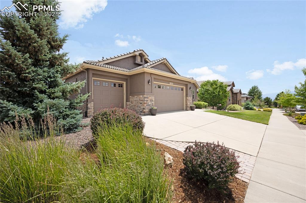 View of front of home with an attached garage, stone siding, concrete driveway, stucco, and a tiled roof