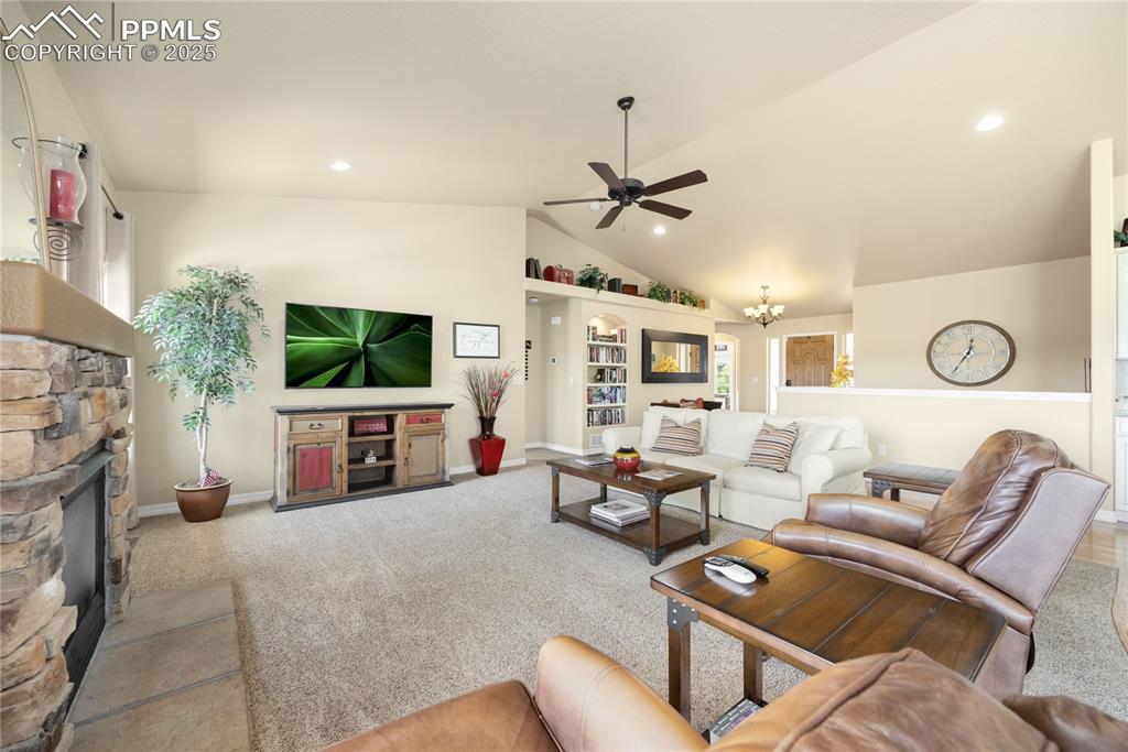 Carpeted living area with ceiling fan, lofted ceiling, a stone fireplace, recessed lighting, and a chandelier