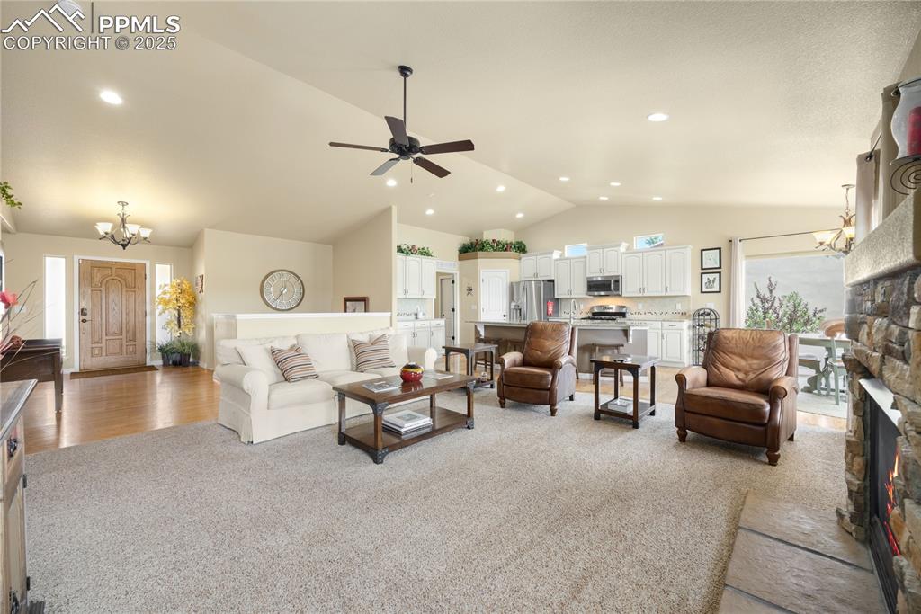 Living area with lofted ceiling, light colored carpet, a stone fireplace, and ceiling fan