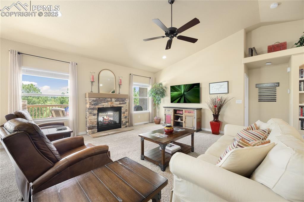 Living room featuring lofted ceiling, carpet floors, a ceiling fan, recessed lighting, and a stone fireplace