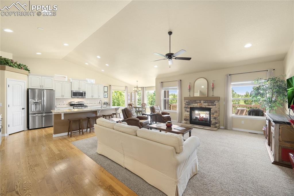 Living area with a ceiling fan, recessed lighting, lofted ceiling, a fireplace, and light wood-type flooring
