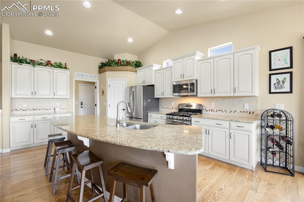 Kitchen featuring stainless steel appliances, a kitchen breakfast bar, light wood-style flooring, white cabinetry, and lofted ceiling