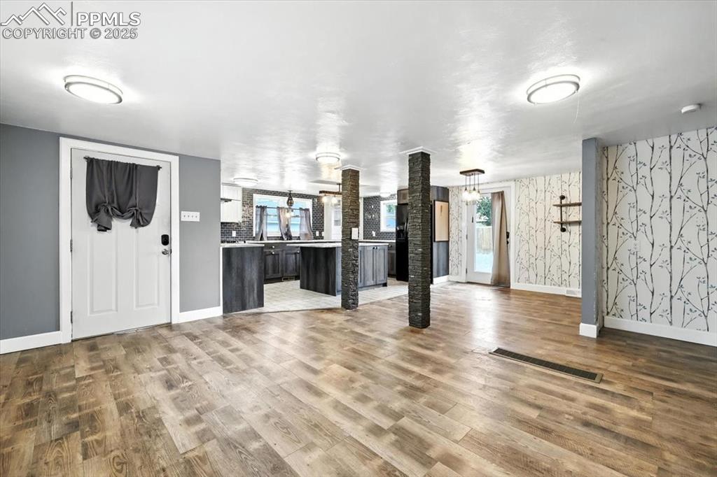Unfurnished living room with ornate columns, wood finished floors, and wallpapered walls
