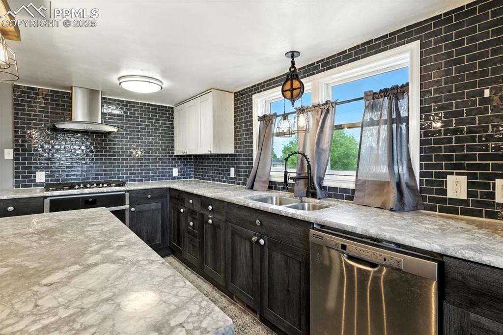 Kitchen with appliances with stainless steel finishes, wall chimney range hood, decorative backsplash, and decorative light fixtures