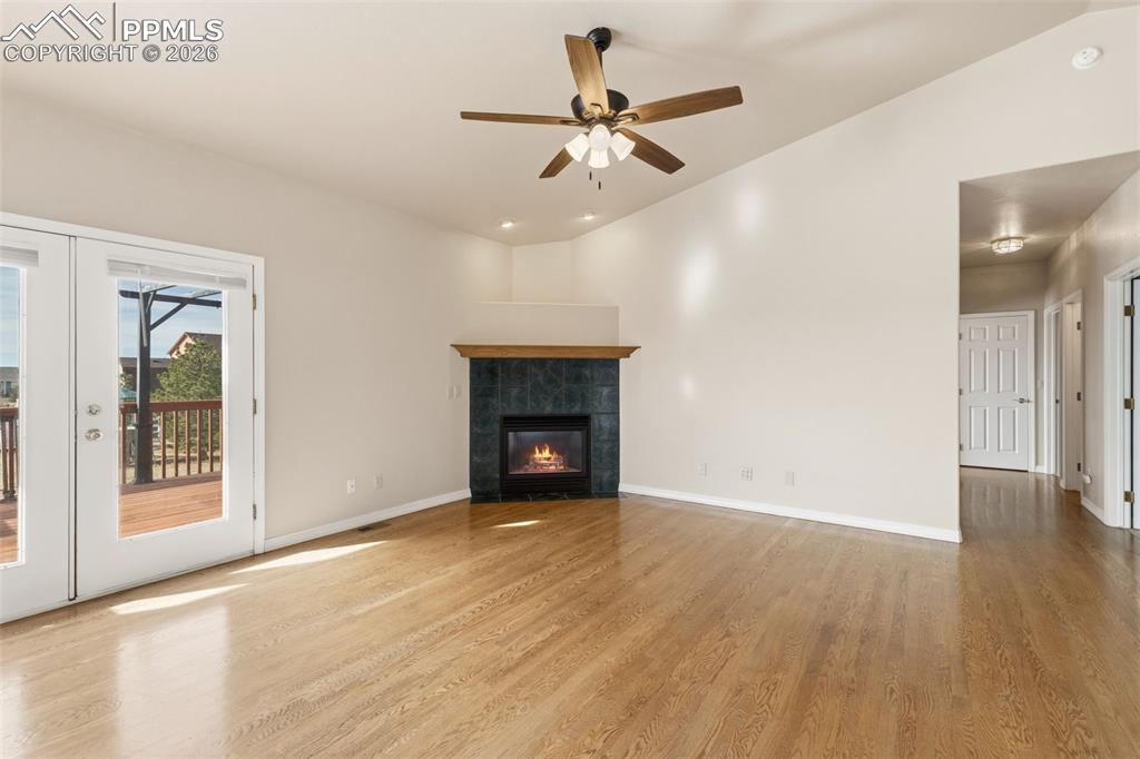 Unfurnished living room with vaulted ceiling, a ceiling fan, light wood-style flooring, a tile fireplace, and french doors