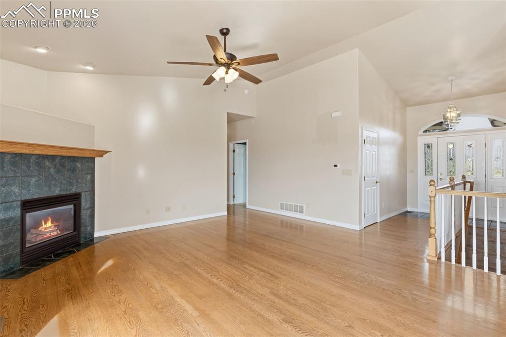 Unfurnished living room featuring light wood-style flooring, a fireplace, a ceiling fan, a chandelier, and vaulted ceiling