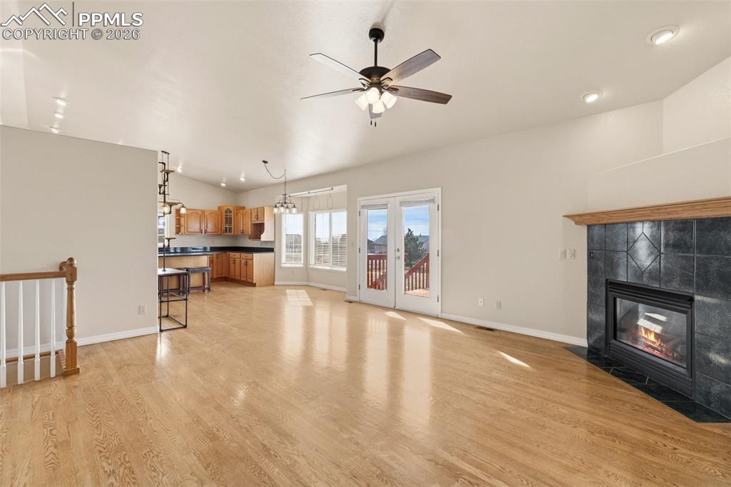 Unfurnished living room with light wood-type flooring, a ceiling fan, a tile fireplace, vaulted ceiling, and recessed lighting