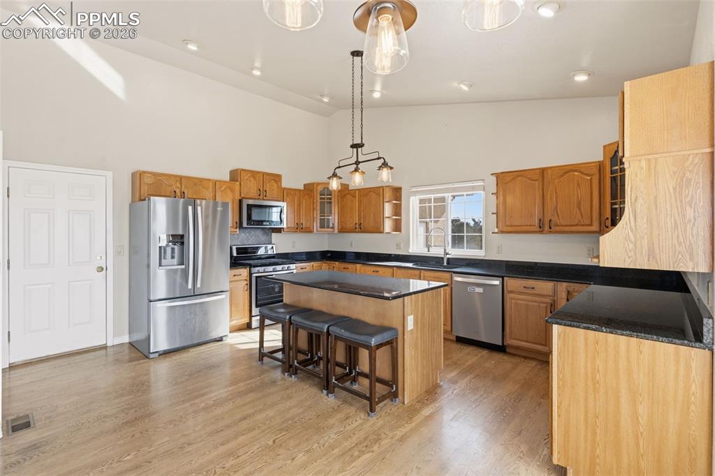 Kitchen with glass insert cabinets, stainless steel appliances, a center island, vaulted ceiling, and a breakfast bar