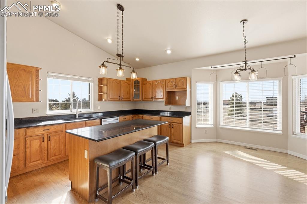 Kitchen with open shelves, a kitchen island, wood finish cabinetry, vaulted ceiling, and glass insert cabinets