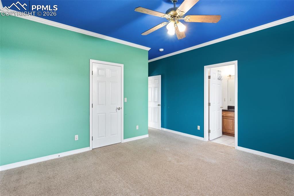 Unfurnished bedroom featuring light colored carpet, ornamental molding, ensuite bath, and ceiling fan