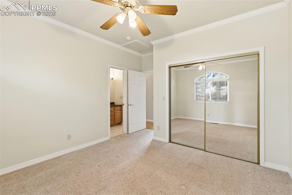 Unfurnished bedroom with crown molding, light carpet, a closet, a ceiling fan, and ensuite bathroom