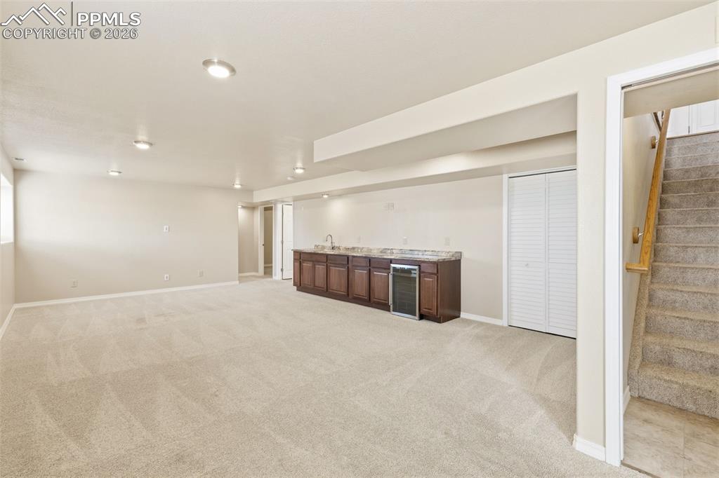 Finished basement featuring bar with sink, light colored carpet, and wine cooler