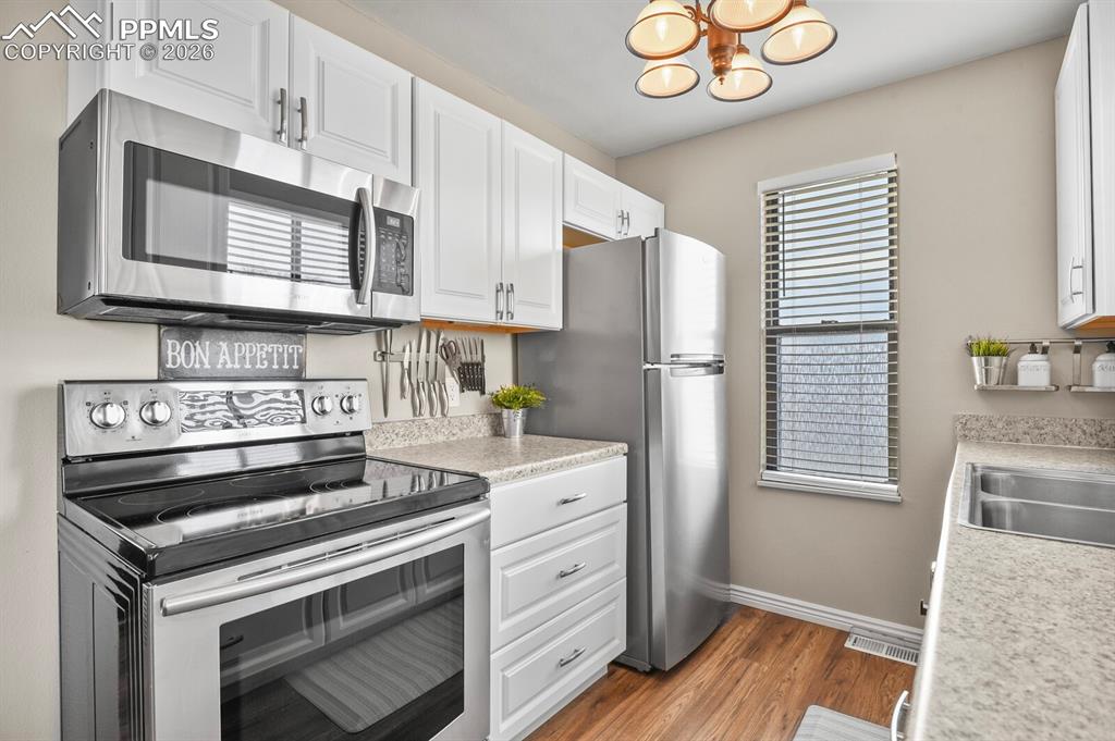 Kitchen with stainless steel appliances, light countertops, white cabinetry, dark wood-style floors, and hanging lights