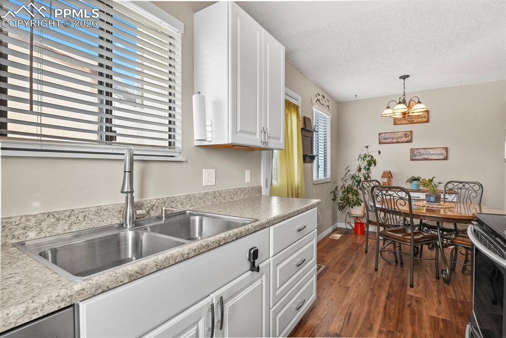 Kitchen with white cabinets, light countertops, dark wood-type flooring, hanging lights, and stainless steel range oven
