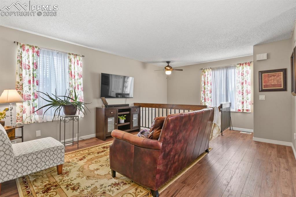 Living room featuring hardwood / wood-style flooring, a textured ceiling, healthy amount of natural light, and a ceiling fan