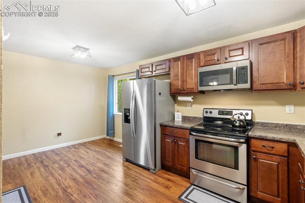 Kitchen with appliances with stainless steel finishes, dark countertops, light wood-style flooring, and brown cabinets