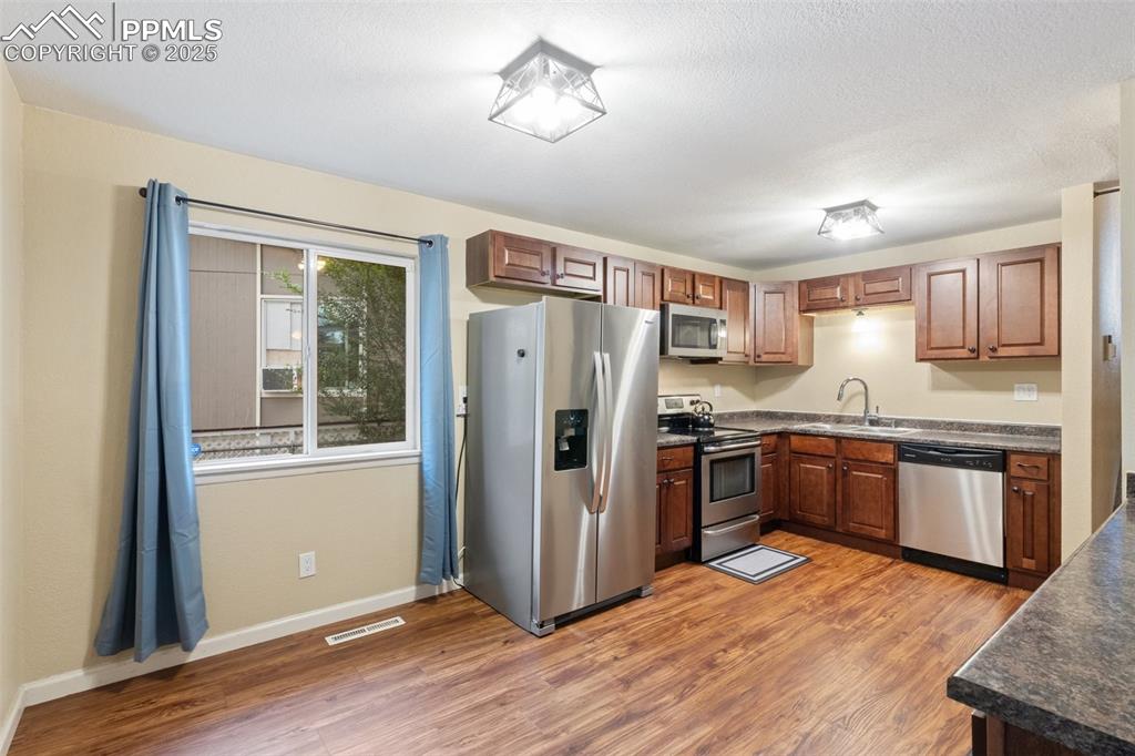 Kitchen with stainless steel appliances, dark countertops, light wood finished floors, and brown cabinets