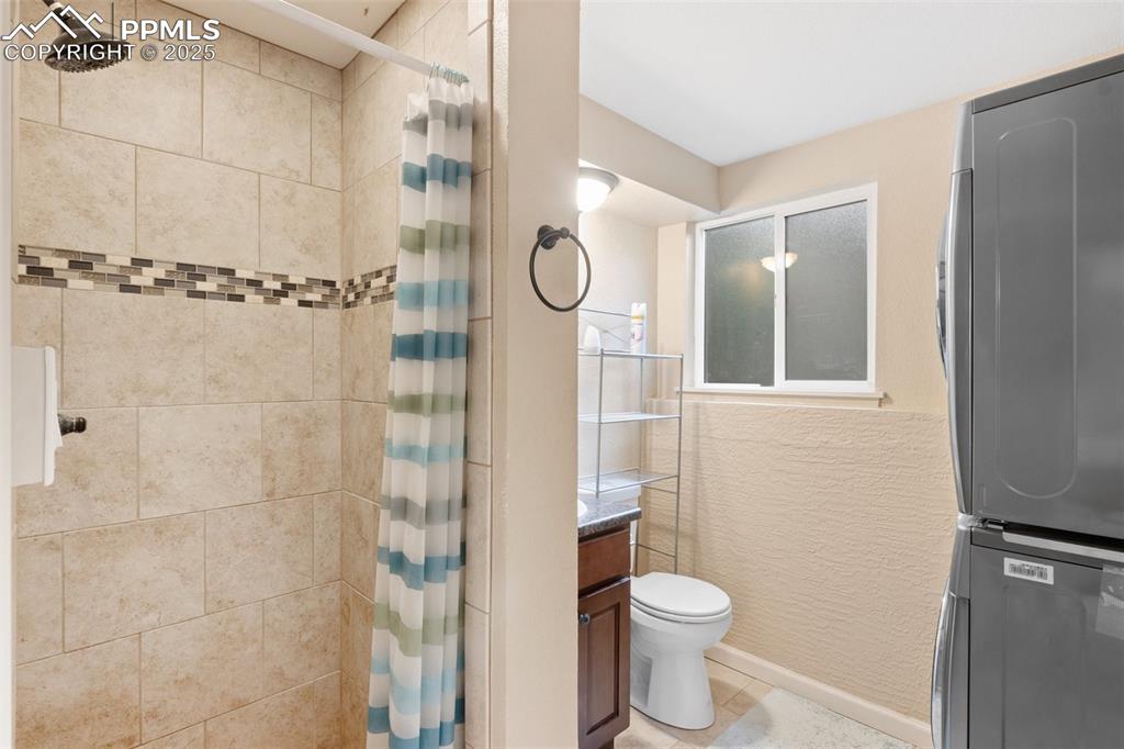 Full bath featuring stacked washer / dryer, tiled shower, tile patterned floors, and vanity