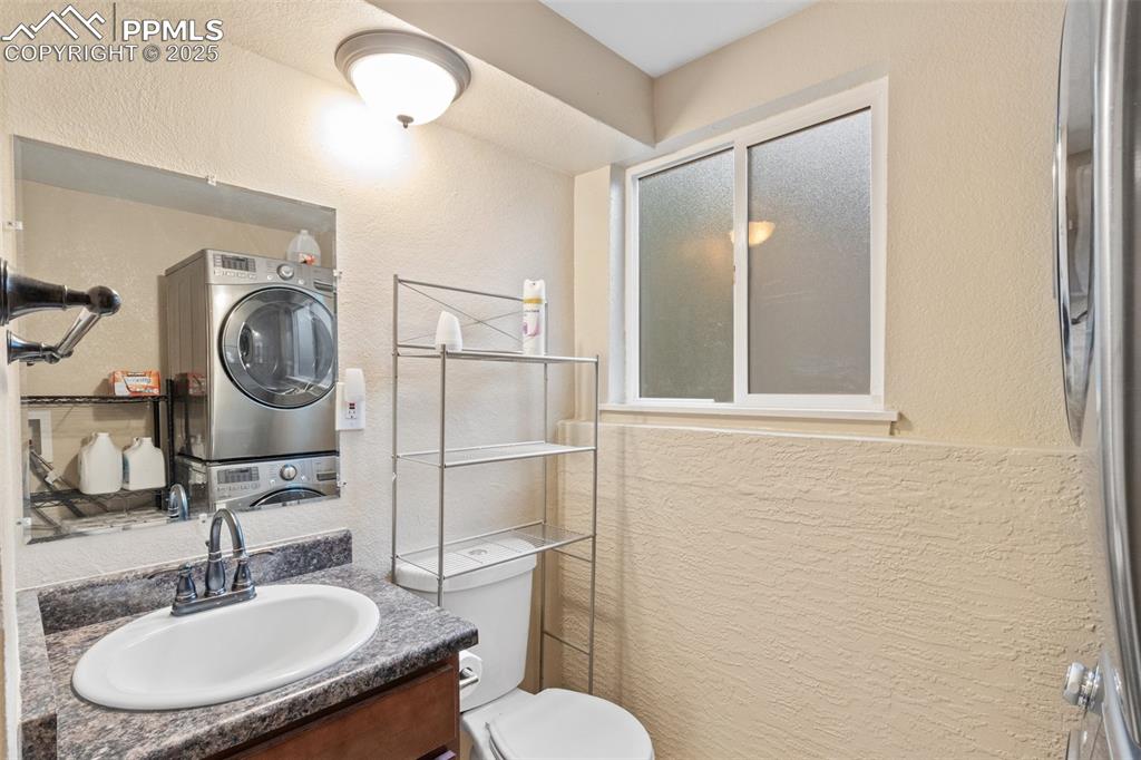 Full bath featuring stacked washing machine and dryer, vanity, a textured wall, and a shower with door
