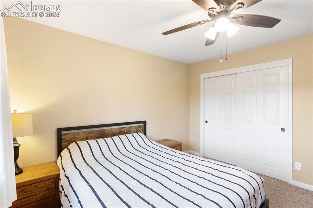 Carpeted bedroom featuring ceiling fan and a closet