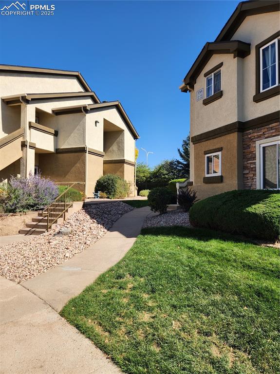 View of side of property featuring stucco siding, stone siding, a yard, and stairway