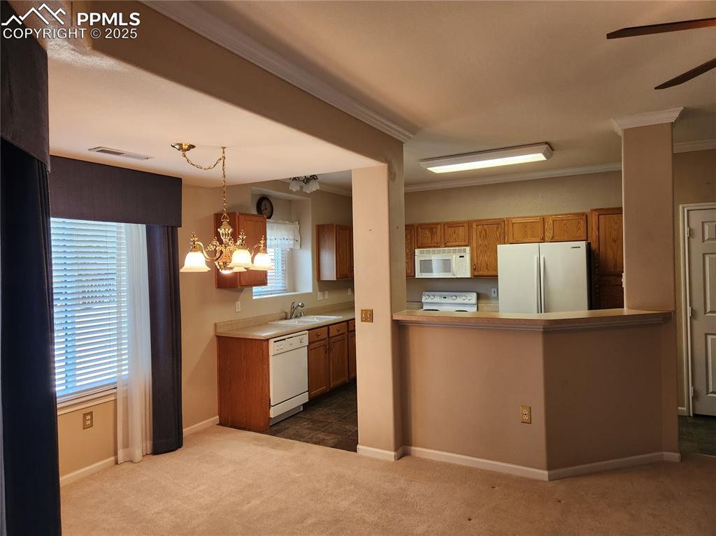 Kitchen with white appliances, brown cabinets, a chandelier, dark colored carpet, and crown molding