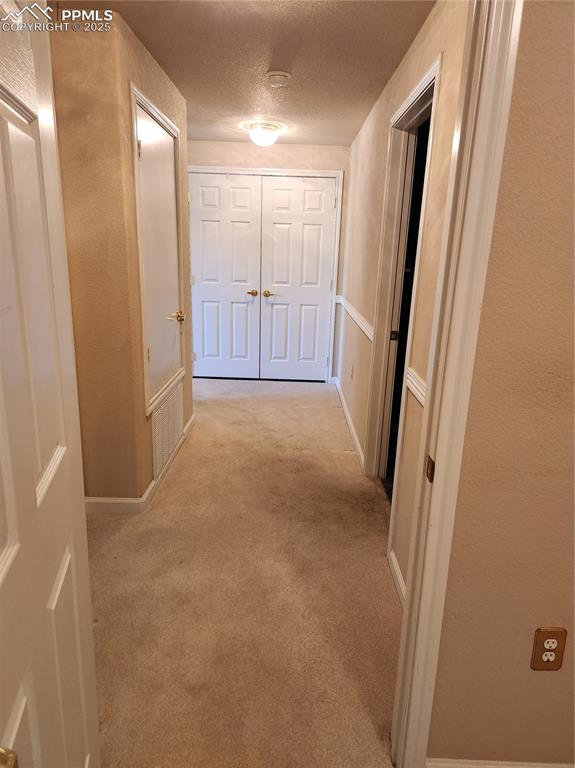 Hall featuring light carpet, a textured ceiling, and a textured wall