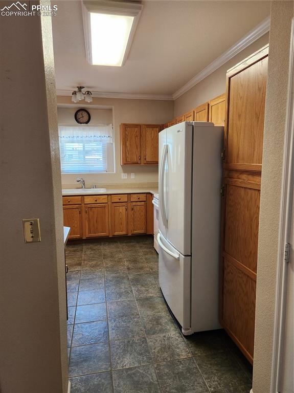 Kitchen featuring fridge, dark stone finish floors, light countertops, ornamental molding, and brown cabinets