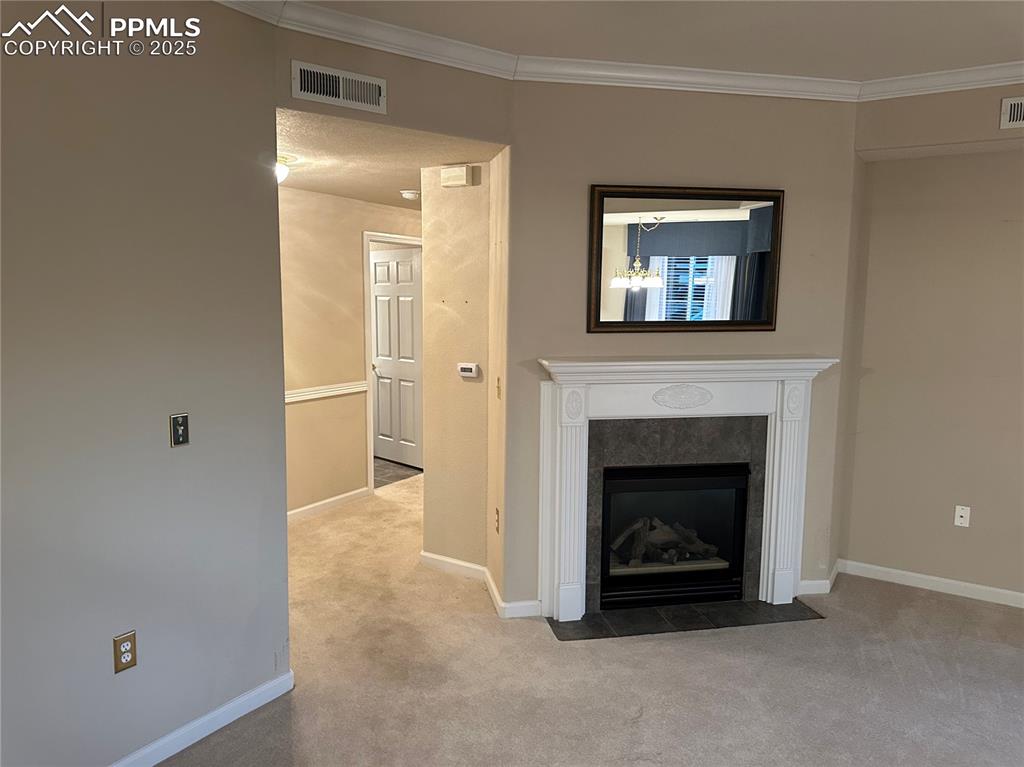 Unfurnished living room featuring carpet floors, crown molding, and a fireplace