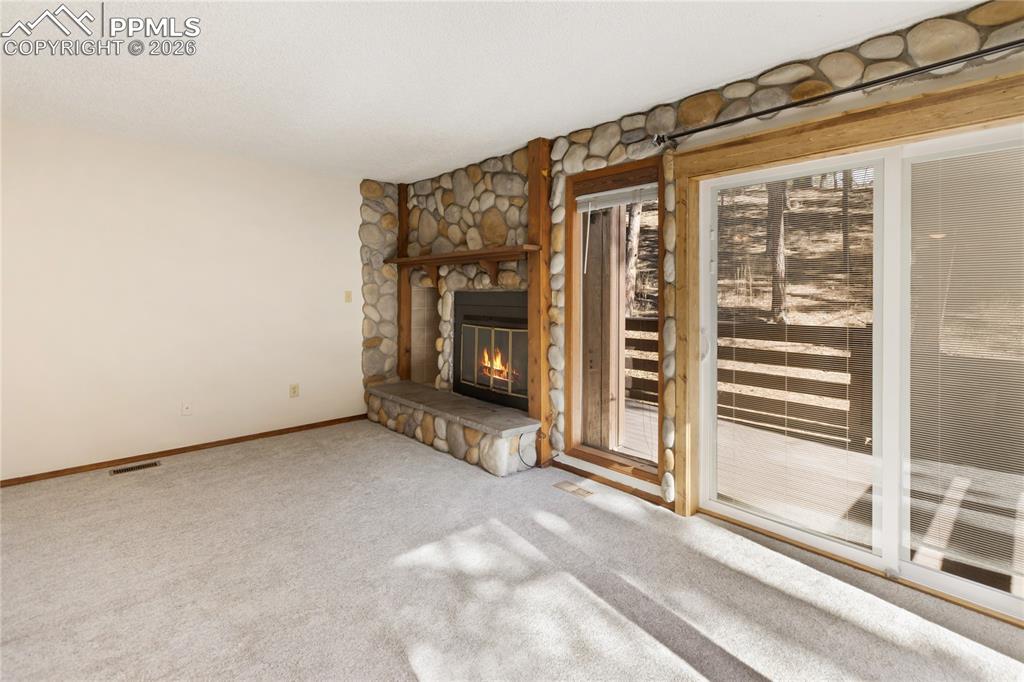 The walkout living room with carpet flooring, a fireplace with stone accents!