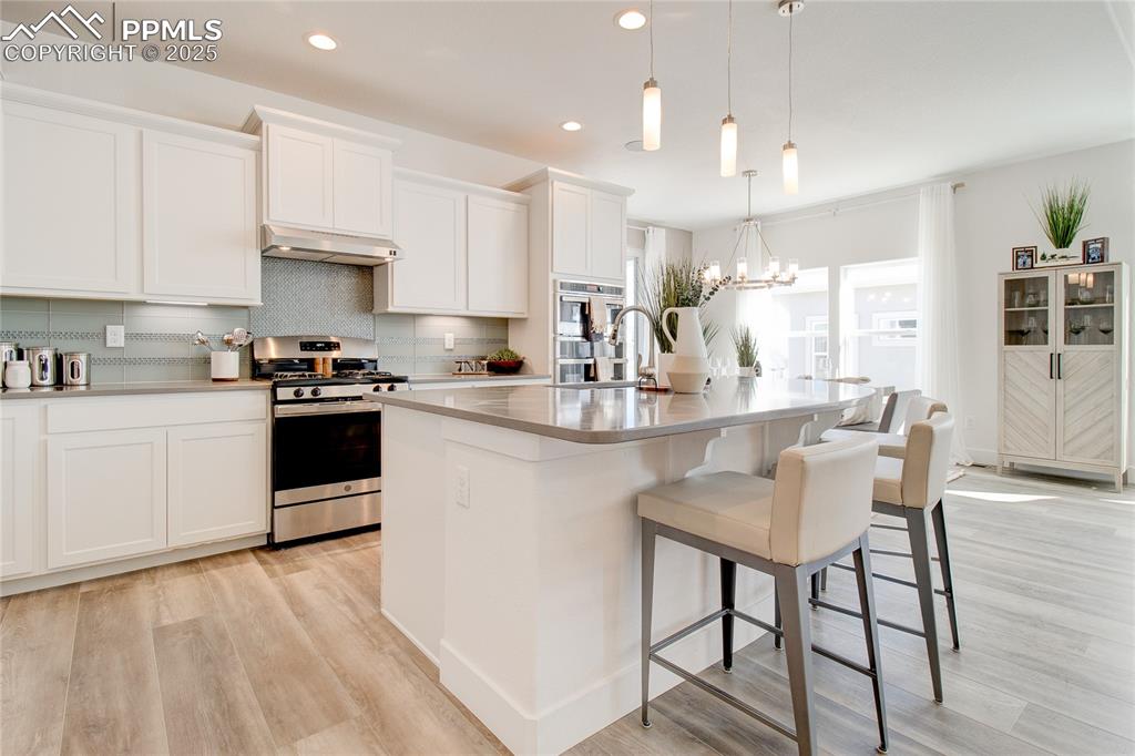 Kitchen featuring appliances with stainless steel finishes, light wood-style floors, decorative backsplash, a kitchen breakfast bar, and recessed lighting
