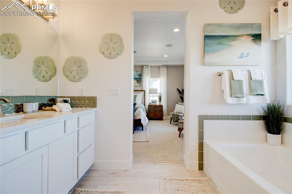 Ensuite bathroom featuring vanity, a bath, wood finished floors, and recessed lighting