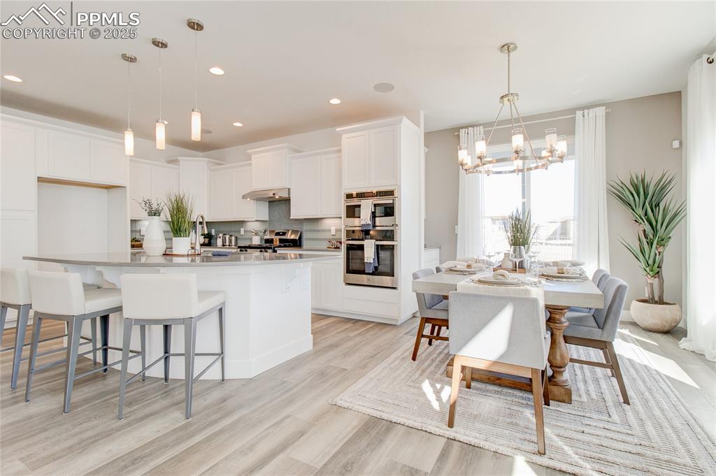 Kitchen featuring a chandelier, decorative backsplash, white cabinets, light wood-style floors, and stainless steel appliances