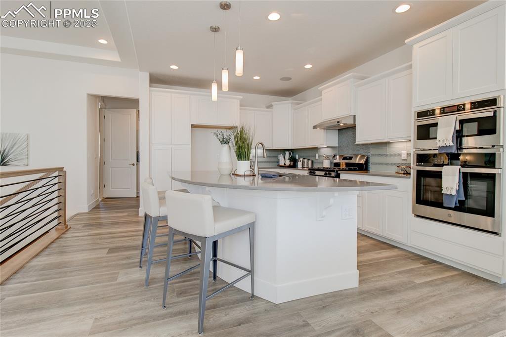 Kitchen with double oven, a kitchen breakfast bar, recessed lighting, stove, and light wood finished floors